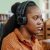 Young Black woman sitting at desk in university library working on desktop computer and listening to music in headphones